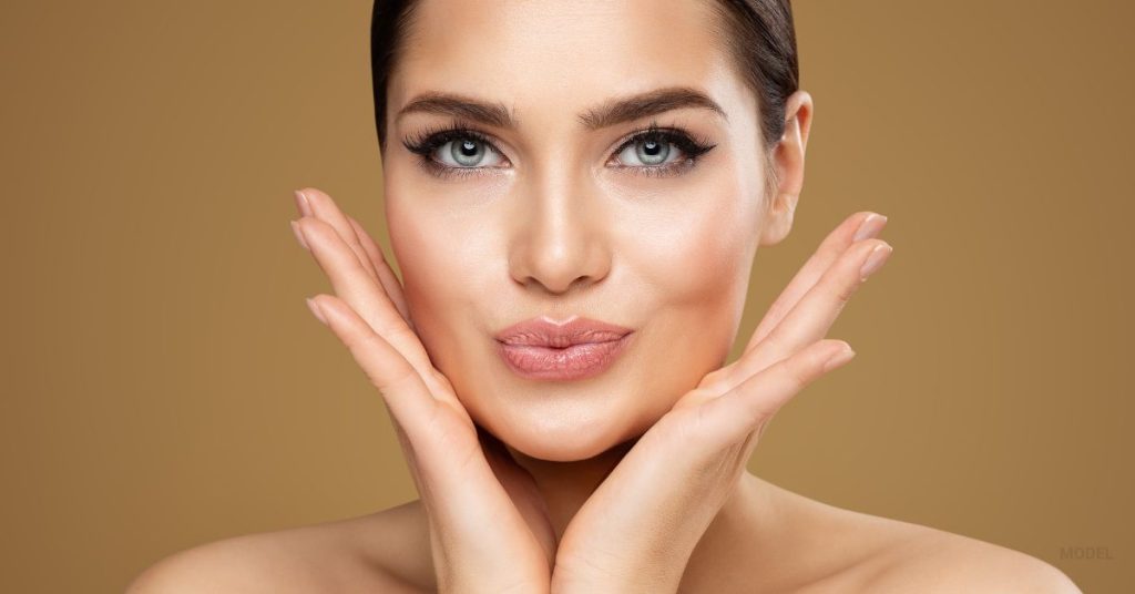 woman holding her cheeks puckering her lips after her lip filler procedure (model)